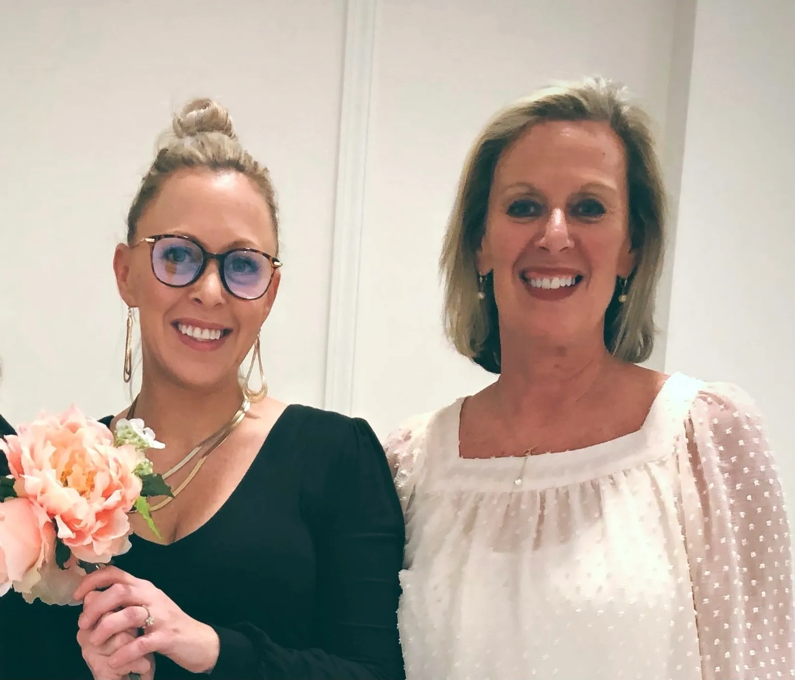 A woman and her mother holding flowers in front of a wall.