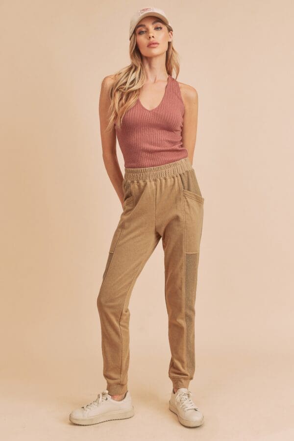 A woman standing in front of a wall wearing tan pants.