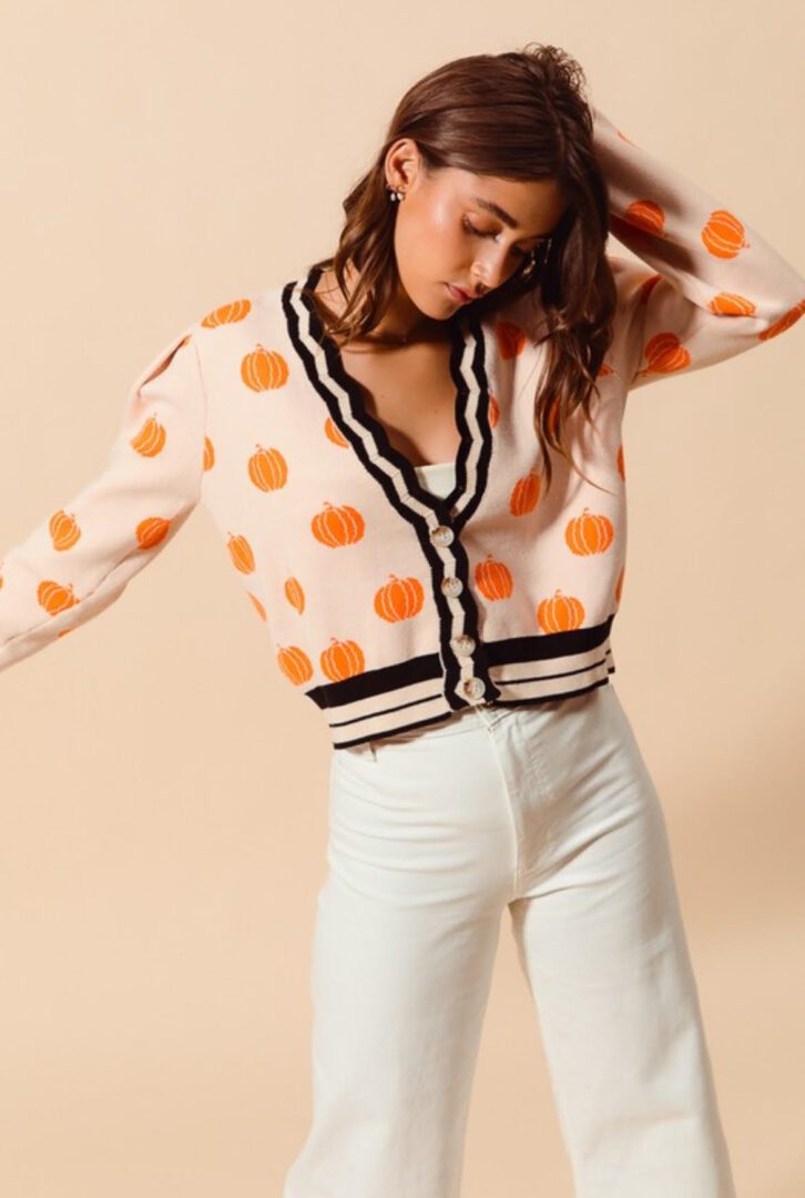 A woman in white pants and orange polka dot sweater.