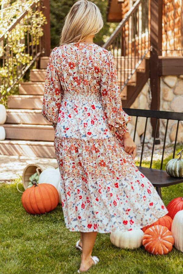 A woman in a floral dress standing next to pumpkins.