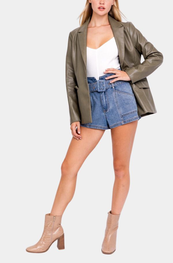 Woman in olive blazer, denim shorts, boots.